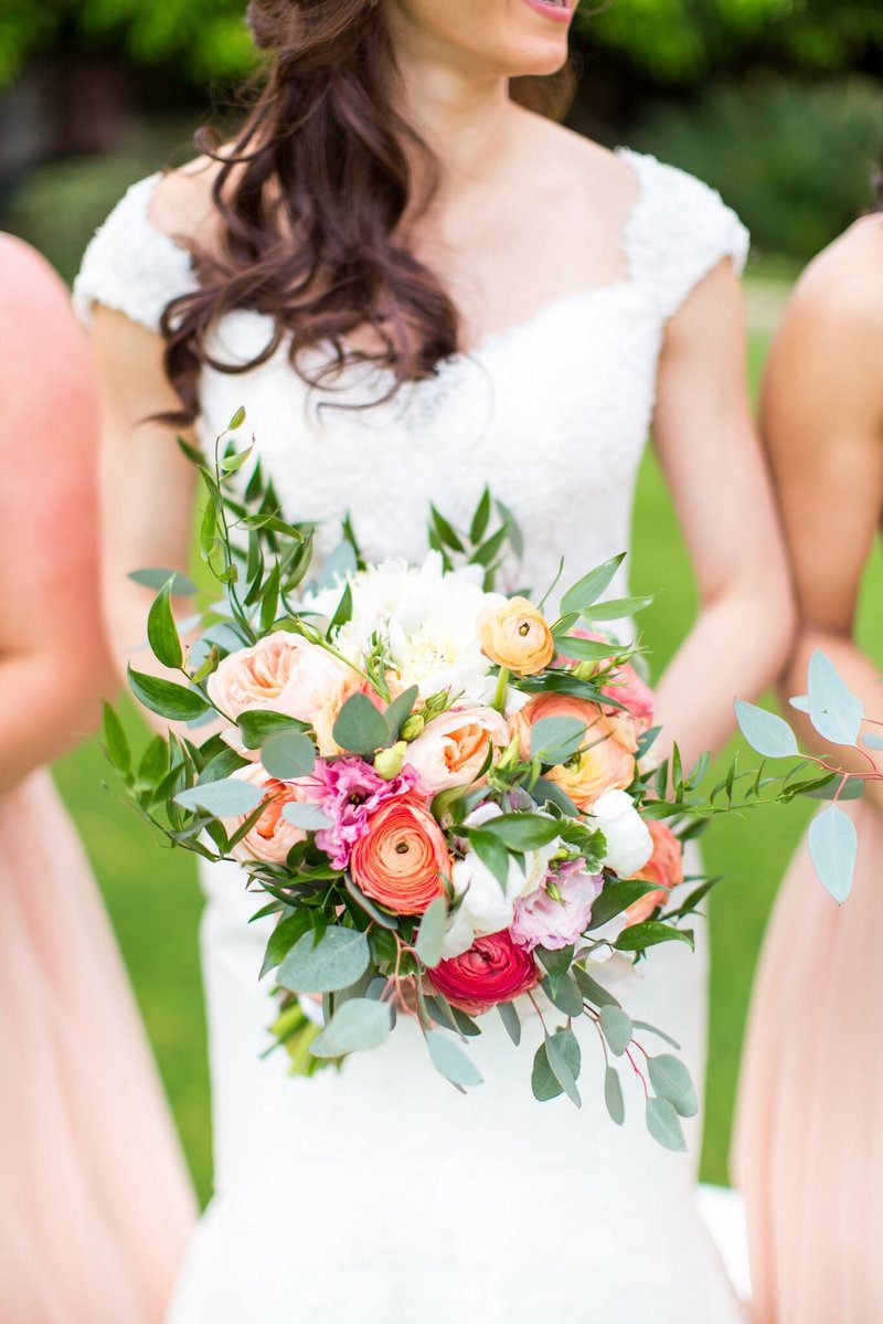 Bride holding colorful bouquet in wedding dress.