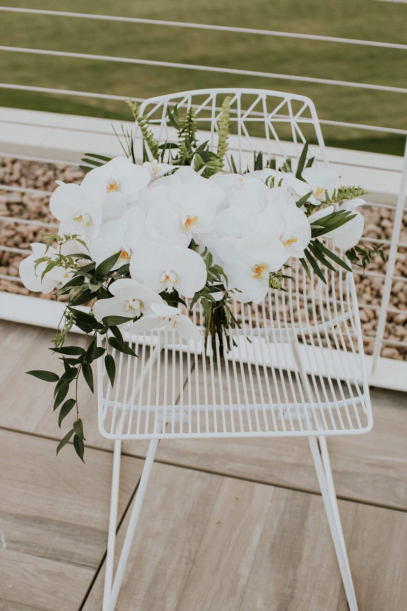 White orchids on a wire chair outdoors.